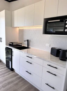 Modern white kitchen renovation with black fixtures, marble countertop, and appliances.