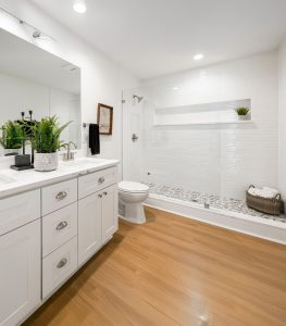Bright, modern bathroom with white cabinets, marble countertop, large mirror, and wooden floor.